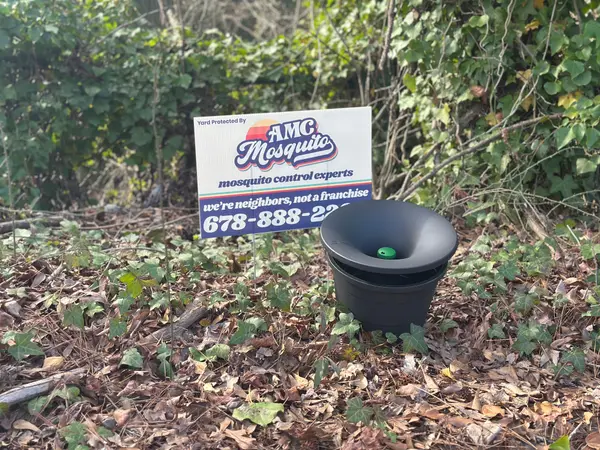 In2Care mosquito station beside an AMC Mosquito Control yard sign in a planting bed.