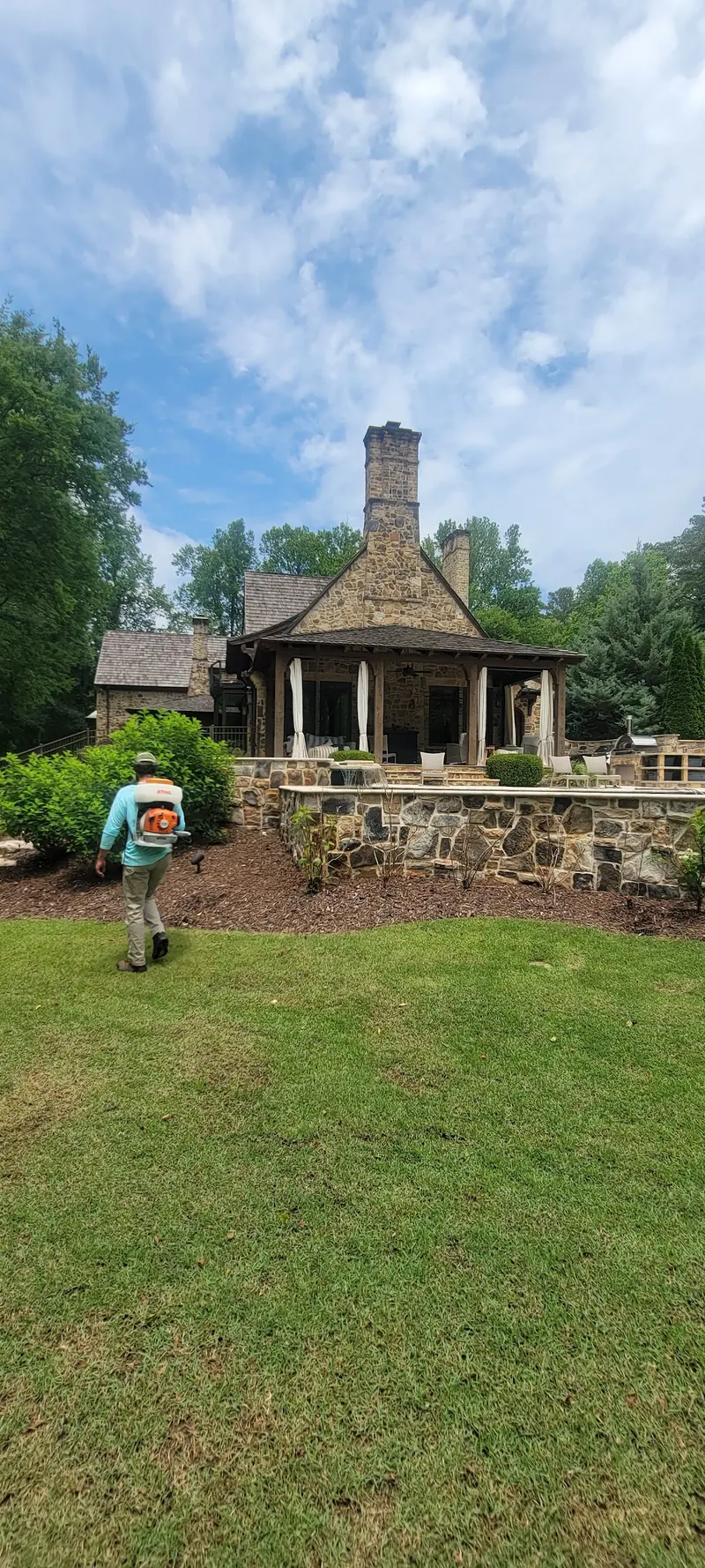 AMC Mosquito technician walking toward landscaped beds beside a stone backyard porch.